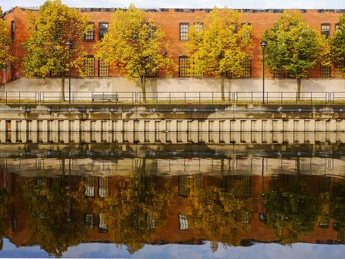 The image is of downtown Flint. There is a stretch of building covered with small trees with a river as the view. 